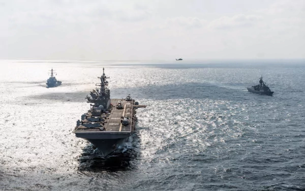 Aerial view of the USS America (LHA-6) amphibious assault ship with helicopters and warships navigating the sea under a bright sky.