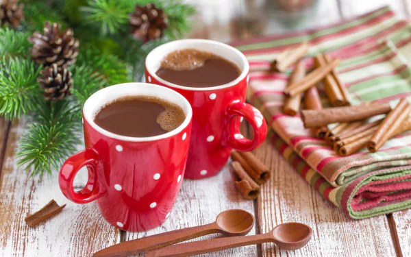 Two red polka dot cups filled with hot chocolate beside cinnamon sticks and a striped cloth, set on a wooden table with pine branches, in an 8K Ultra HD desktop wallpaper.