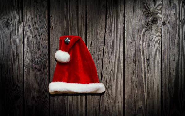 Red Santa hat with white trim on dark wooden planks — festive Christmas holiday 4K Ultra HD PC desktop wallpaper background.