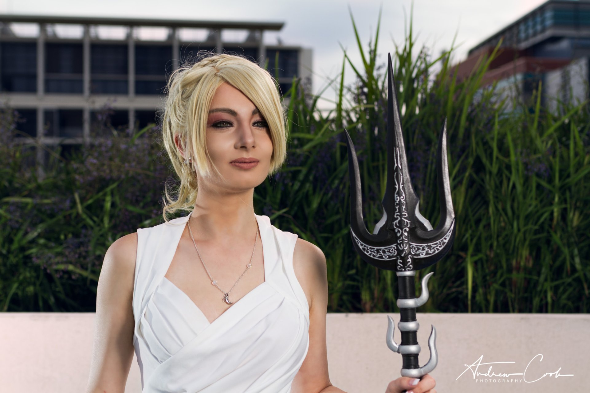 HD PC desktop wallpaper of a woman in Final Fantasy cosplay: blonde in a white dress holding an ornate trident against an urban greenery backdrop.