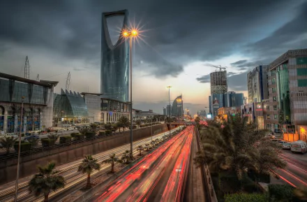 Time lapse view of Riyadh’s skyline at dusk with streaks of red car lights and modern man-made skyscrapers under a moody sky, captured in HD for a desktop wallpaper.