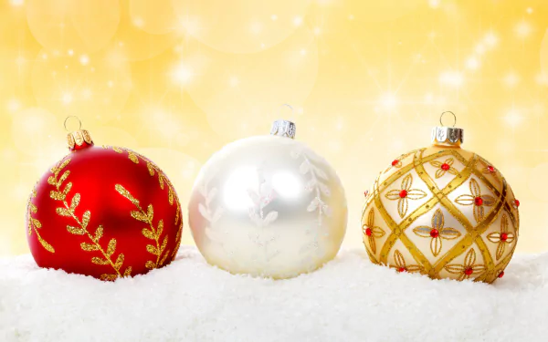 HD desktop wallpaper featuring three Christmas ornaments — a red, white, and gold bauble — resting on snow with a glowing golden holiday background.