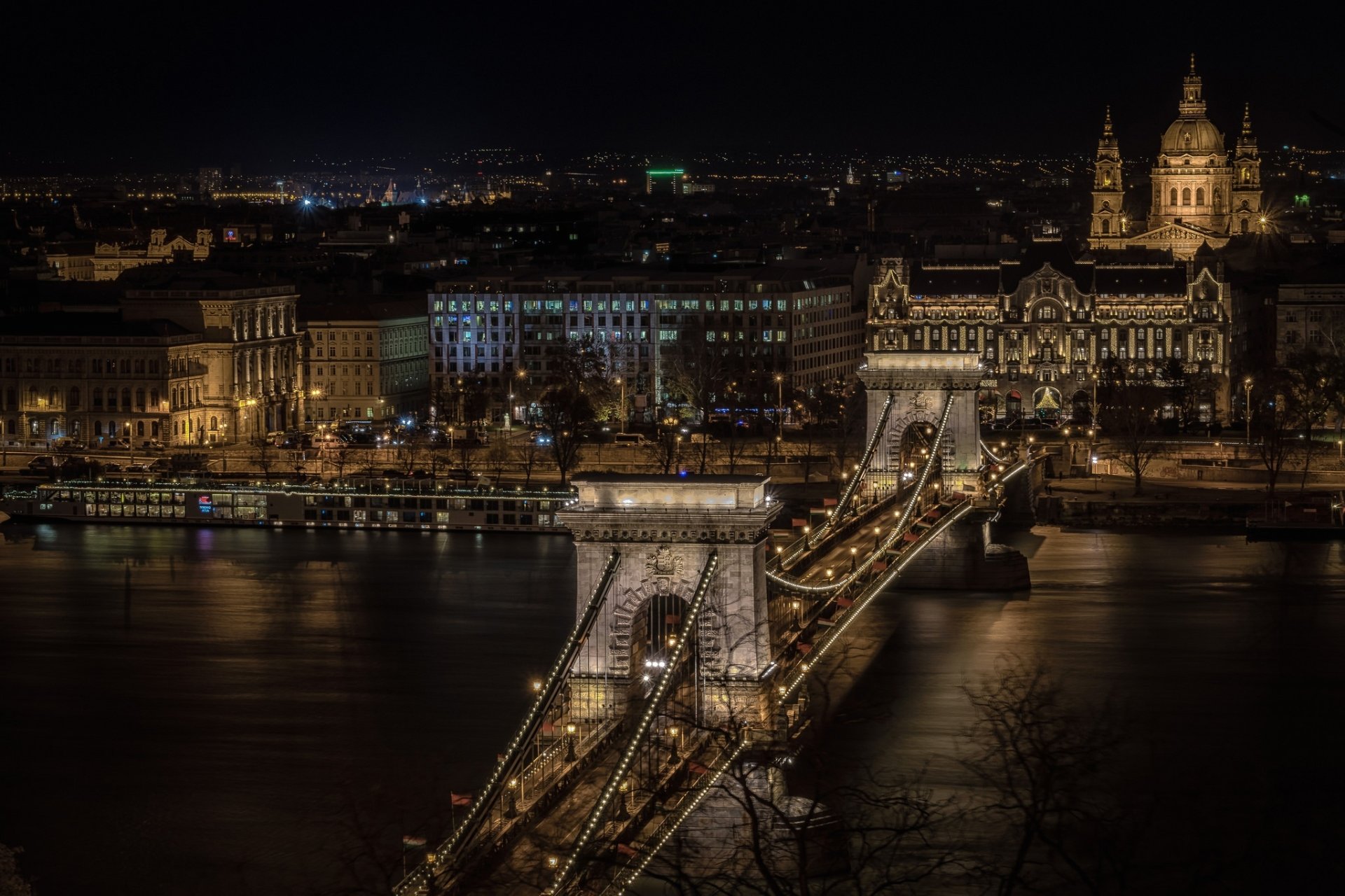 Night view of Budapest's Chain Bridge illuminated over the Danube River, showcasing the city's historic architecture along the riverbank in Hungary.
