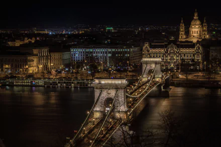 Night view of Budapest's Chain Bridge illuminated over the Danube River, showcasing the city's historic architecture along the riverbank in Hungary.