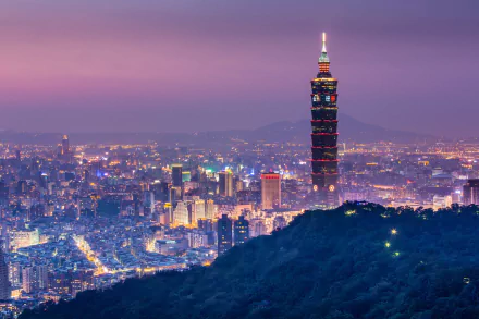 HD desktop wallpaper featuring the illuminated Taipei 101 skyscraper towering over the vibrant cityscape of Taipei at dusk, with the soft glow of city lights and the surrounding landscape enhancing the view.
