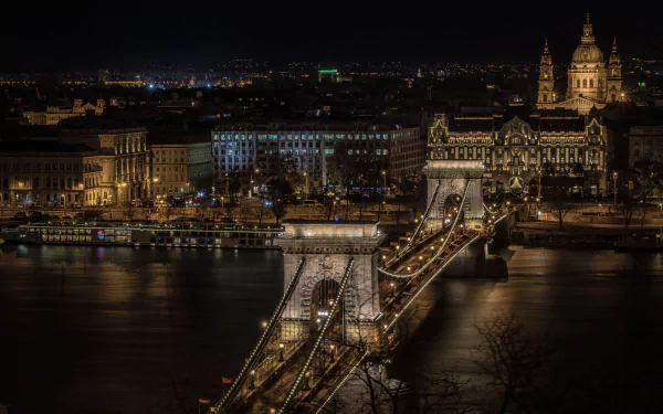 Night view of Budapest's Chain Bridge illuminated over the Danube River, showcasing the city's historic architecture along the riverbank in Hungary.