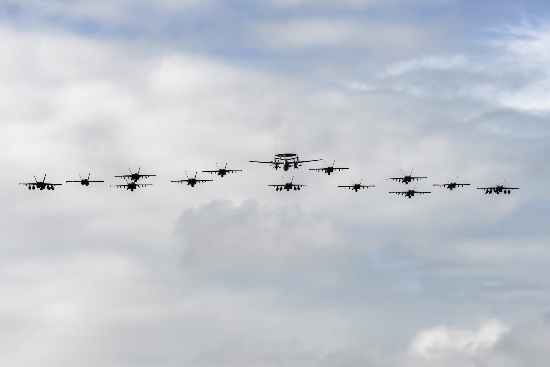 HD PC desktop wallpaper showing a formation of military jet fighters and warplanes flying together during an air show against a cloudy sky background.