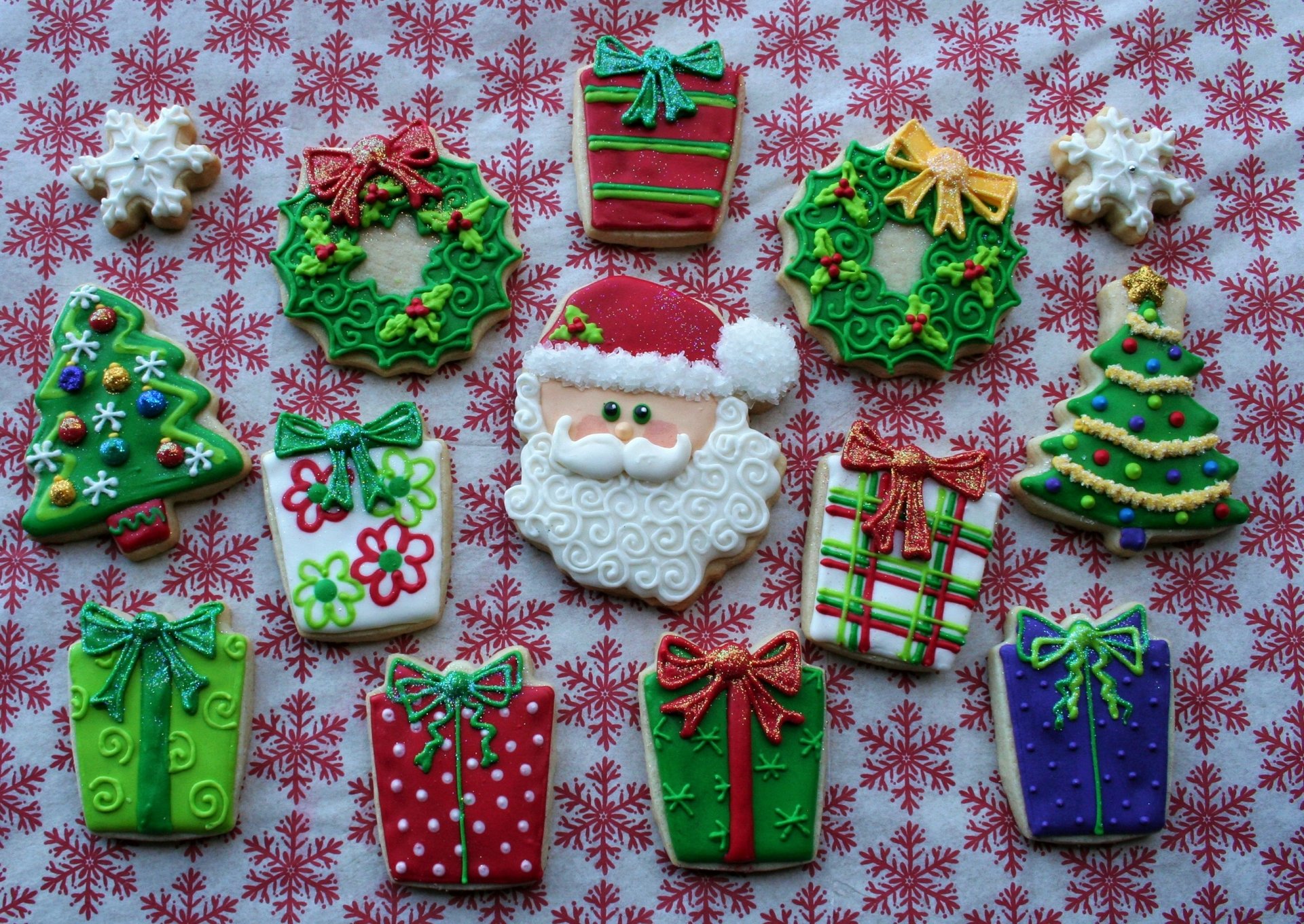 Colorful Christmas-themed cookies shaped like Santa, wreaths, trees, and gifts arranged on a festive red and white snowflake-patterned background, HD desktop wallpaper.