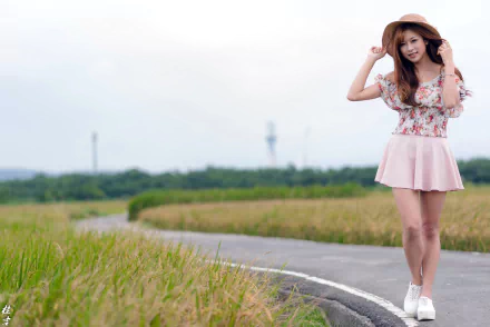 Brunette model wearing a hat and pink skirt poses on a winding road with shallow depth of field — 2K Quad HD PC desktop wallpaper/background.