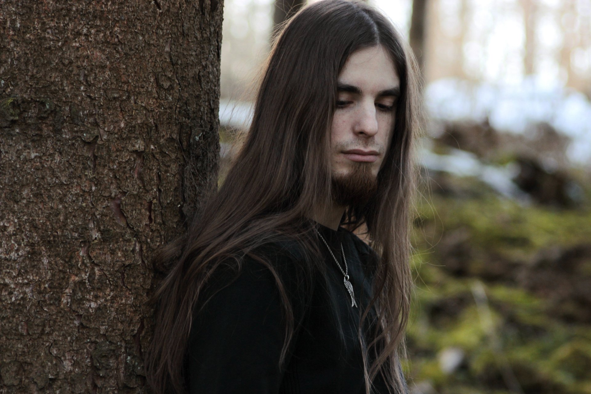 HD PC desktop wallpaper featuring musician Adrian von Ziegler with long hair, standing thoughtfully against a tree in a natural, wooded background.