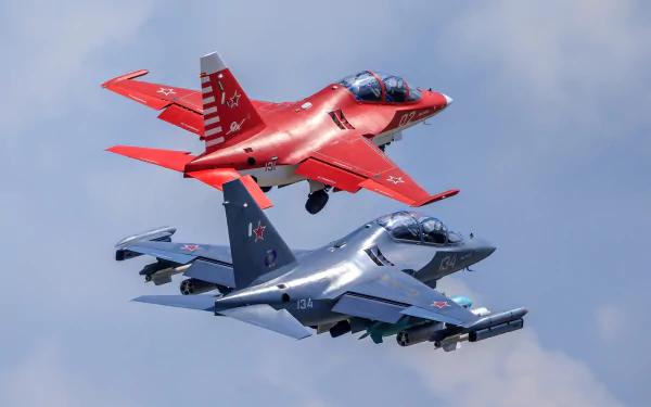 Two Yakovlev Yak-130 jet fighter warplanes, one red and one gray, fly closely against a blue sky in this HD military aircraft wallpaper.