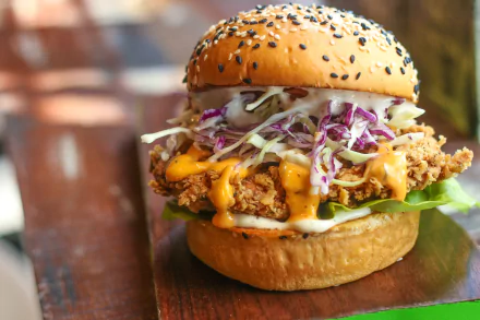 HD PC desktop wallpaper of a hamburger/burger: crispy fried patty in a sesame bun with melted cheese, slaw and lettuce — lunch meal food background.