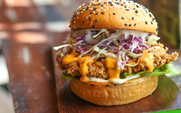 HD PC desktop wallpaper of a hamburger/burger: crispy fried patty in a sesame bun with melted cheese, slaw and lettuce — lunch meal food background.