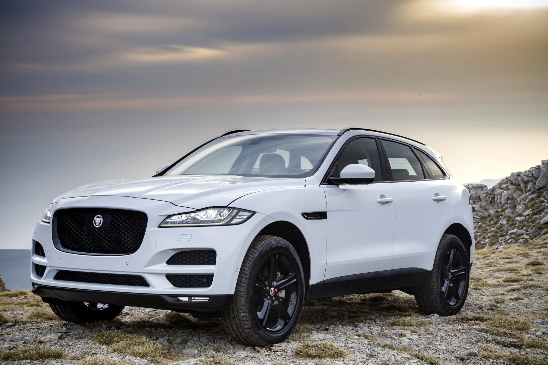 White Jaguar F-PACE SUV parked on rocky terrain under a cloudy sky, showcased as a high-definition desktop wallpaper background.