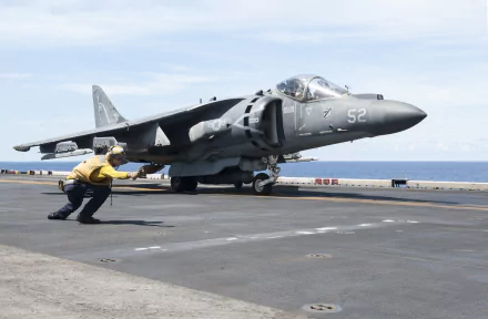 McDonnell Douglas AV-8B Harrier II warplane jet fighter on aircraft carrier deck, with crew member guiding; military aircraft in HD desktop wallpaper quality.