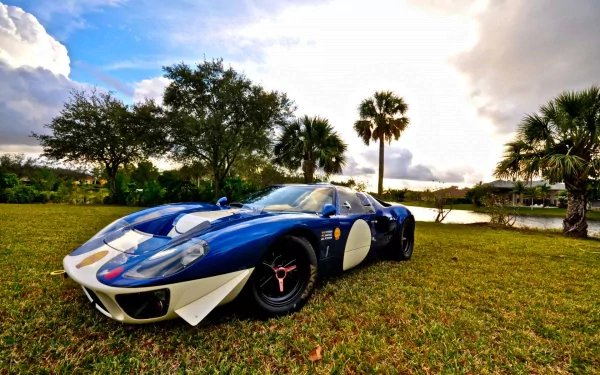 HD desktop wallpaper featuring a blue Ford GT40 Mk II sports car parked on grass with trees and a partly cloudy sky in the background.