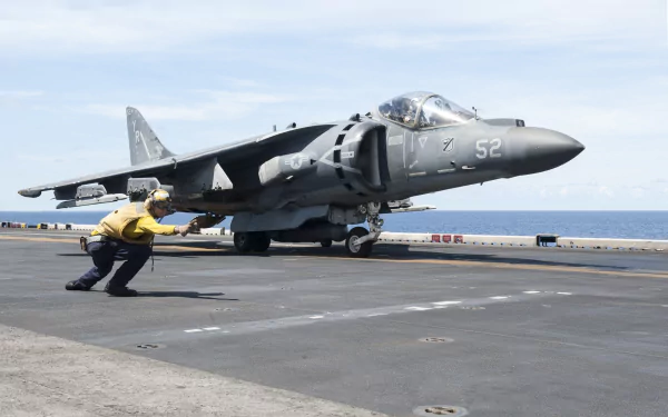 McDonnell Douglas AV-8B Harrier II warplane jet fighter on aircraft carrier deck, with crew member guiding; military aircraft in HD desktop wallpaper quality.