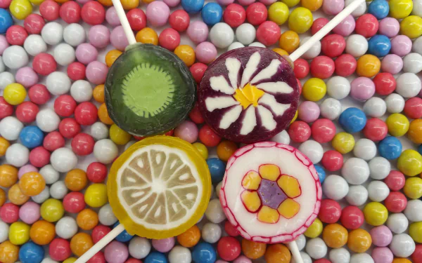 Colorful lollipops with fruit and floral designs rest on a vibrant bed of multicolored candy spheres in this 4K Ultra HD sweets-themed desktop wallpaper.