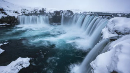 Winter view of the icy Goðafoss waterfall in Iceland, surrounded by snow-covered rocks and flowing water, captured in stunning HD for a nature-inspired desktop wallpaper.