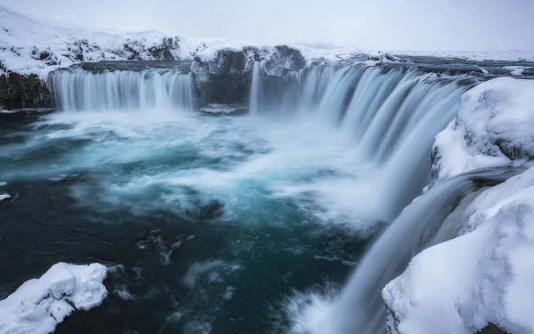 Winter view of the icy Goðafoss waterfall in Iceland, surrounded by snow-covered rocks and flowing water, captured in stunning HD for a nature-inspired desktop wallpaper.