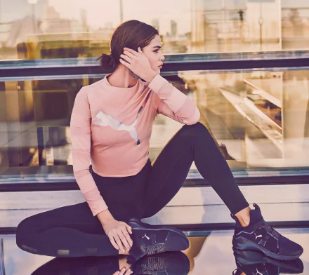 Brunette singer and actress Selena Gomez in Puma activewear, posing thoughtfully in a modern urban setting, captured in a 4K Ultra HD PC wallpaper image.