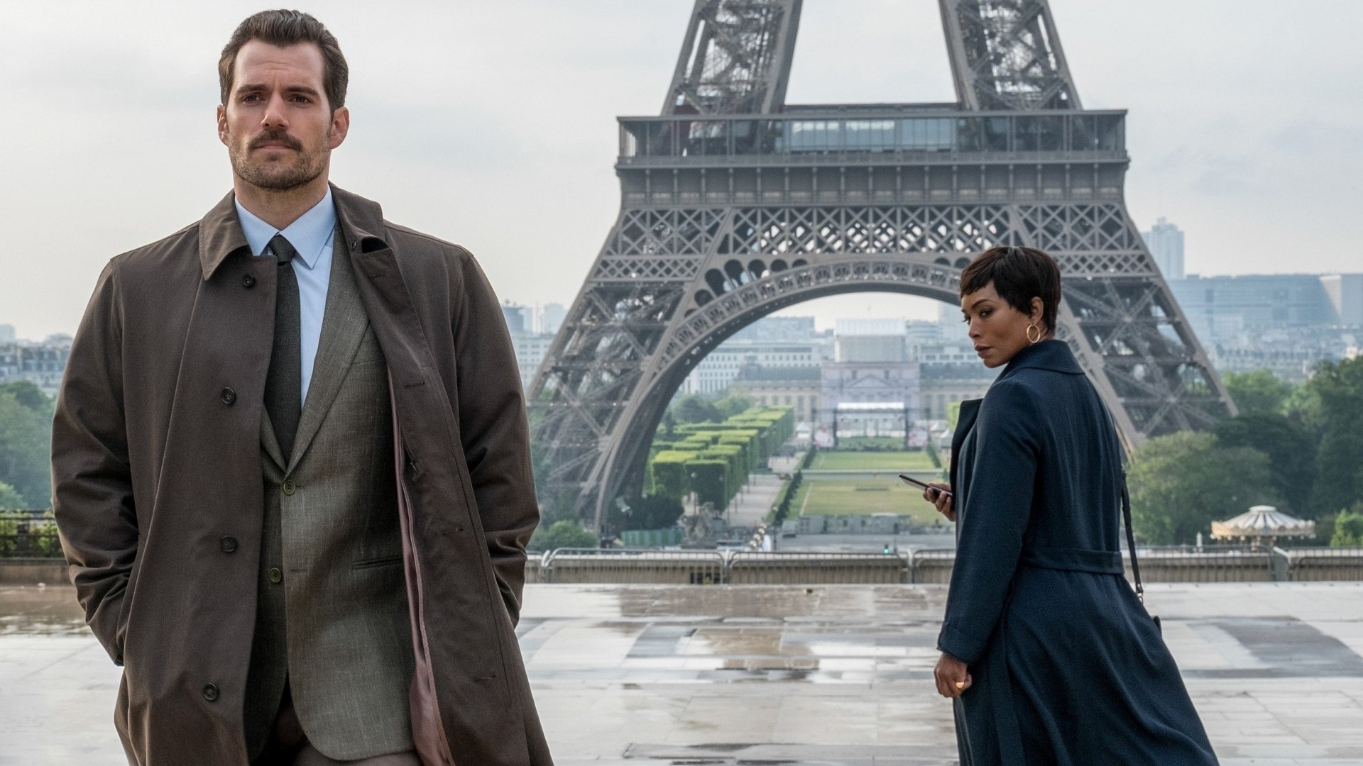 Henry Cavill and a co-star stand in front of the Eiffel Tower in a scene from Mission: Impossible - Fallout, featured in an HD PC desktop wallpaper.