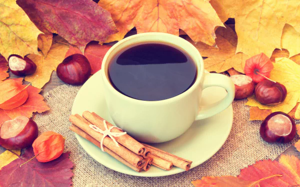 A 4K Ultra HD desktop wallpaper showing a cup of coffee with cinnamon sticks on a saucer, surrounded by colorful autumn leaves and chestnuts.