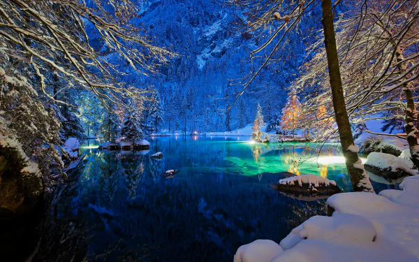 HD wallpaper of a serene, snowy night scene at a lake in Switzerland, surrounded by trees and illuminated by lights. The tranquil water and winter landscape create a peaceful nature setting.