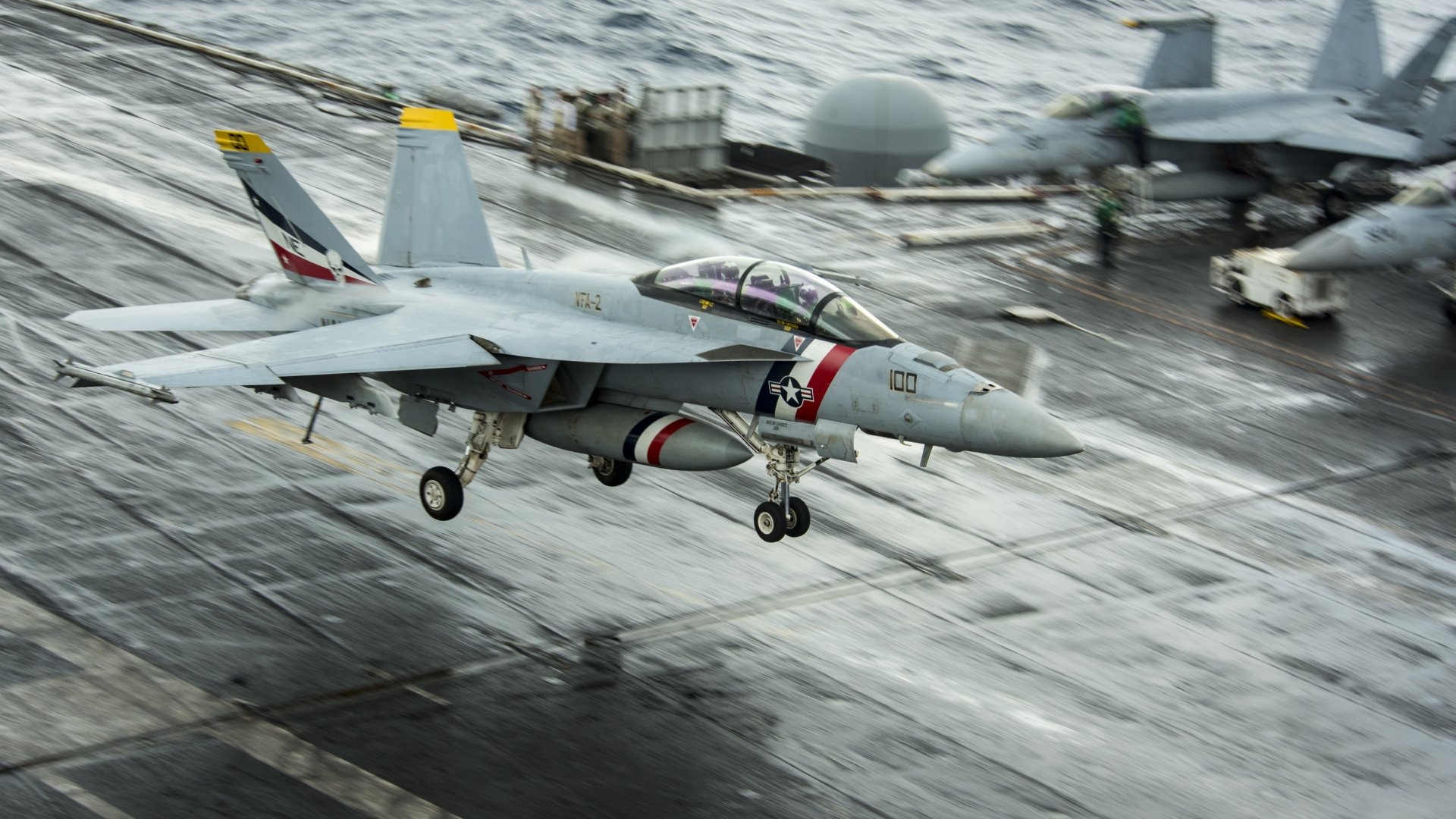 An HD desktop wallpaper of a McDonnell Douglas F/A-18 Hornet jet fighter taking off from an aircraft carrier, with another warplane visible in the background. The military aircraft is in action over the ocean.