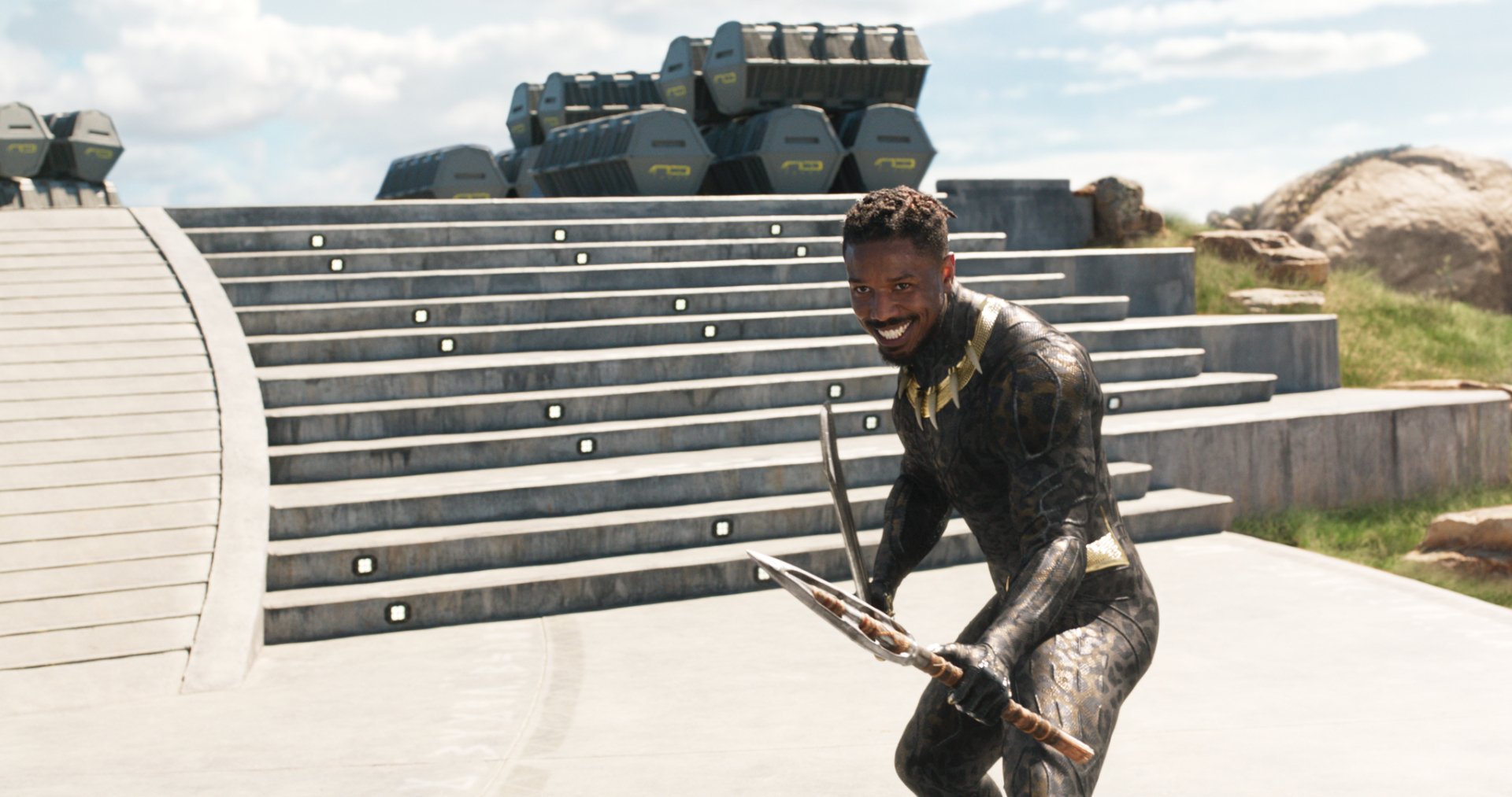 Erik Killmonger from the Black Panther movie posed on steps with weapons, smiling in armor — cinematic HD PC desktop wallpaper and background