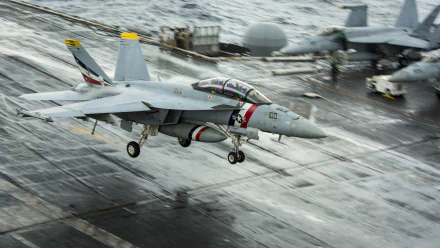 An HD desktop wallpaper of a McDonnell Douglas F/A-18 Hornet jet fighter taking off from an aircraft carrier, with another warplane visible in the background. The military aircraft is in action over the ocean.