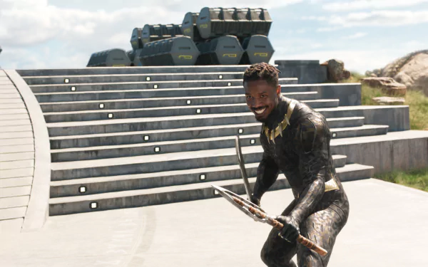 Erik Killmonger from the Black Panther movie posed on steps with weapons, smiling in armor — cinematic HD PC desktop wallpaper and background