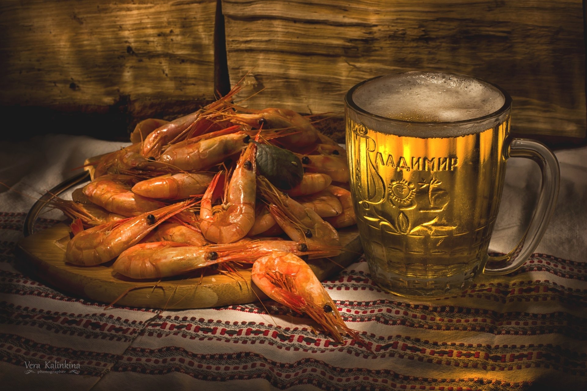 A rustic scene with a glass of beer next to a plate of cooked shrimp, highlighting seafood and drink in a warm, inviting setting.