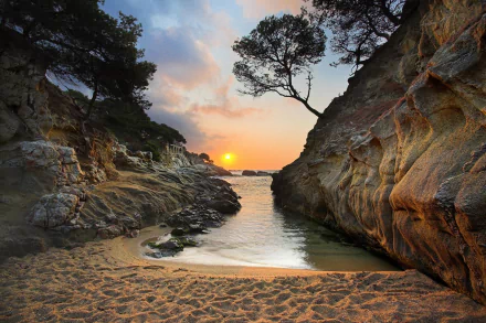 A stunning HD desktop wallpaper of a sunset over a sandy beach in Greece, with a serene coastline, rocky formations, trees, and the sea meeting the horizon.