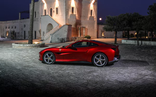 A red Ferrari Portofino supercar parked at night near a historic building, captured in 4K Ultra HD as a striking grand tourer vehicle wallpaper.