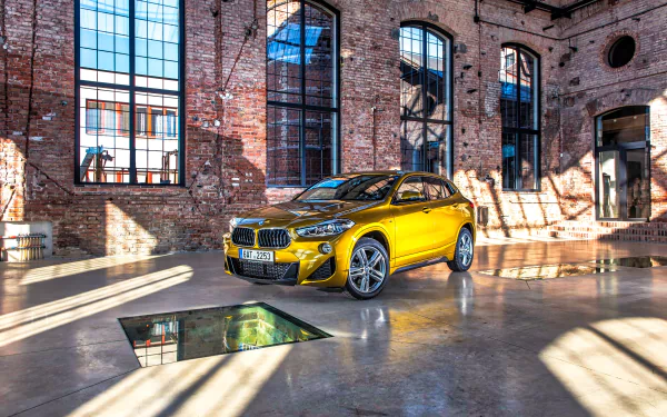 Yellow BMW X2 SUV in a sunlit industrial loft, glossy reflections on polished concrete — high-detail 2K Quad HD desktop wallpaper.