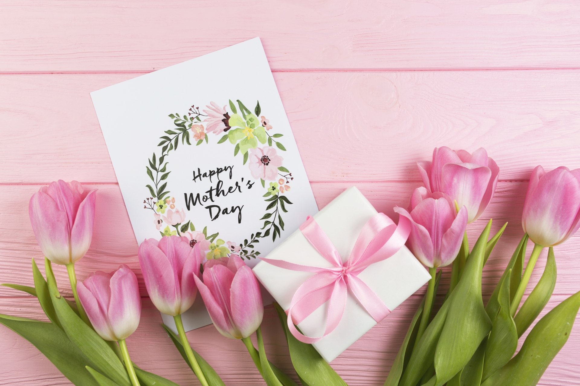 Pink tulips, a white gift box with a pink ribbon, and a Mother's Day card arranged on a pink wooden background; 4K Ultra HD desktop wallpaper.