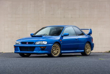 Blue Subaru Impreza with gold wheels parked before a beige wall — car/vehicle image, 2K Quad HD PC Desktop Wallpaper and Background
