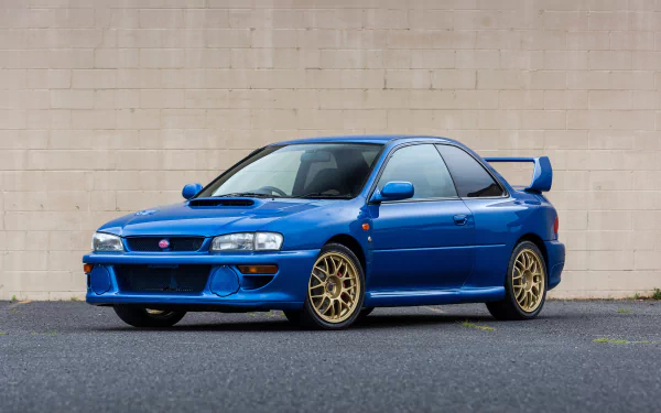 Blue Subaru Impreza with gold wheels parked before a beige wall — car/vehicle image, 2K Quad HD PC Desktop Wallpaper and Background
