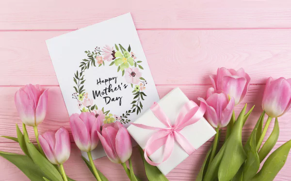 Pink tulips, a white gift box with a pink ribbon, and a Mother's Day card arranged on a pink wooden background; 4K Ultra HD desktop wallpaper.