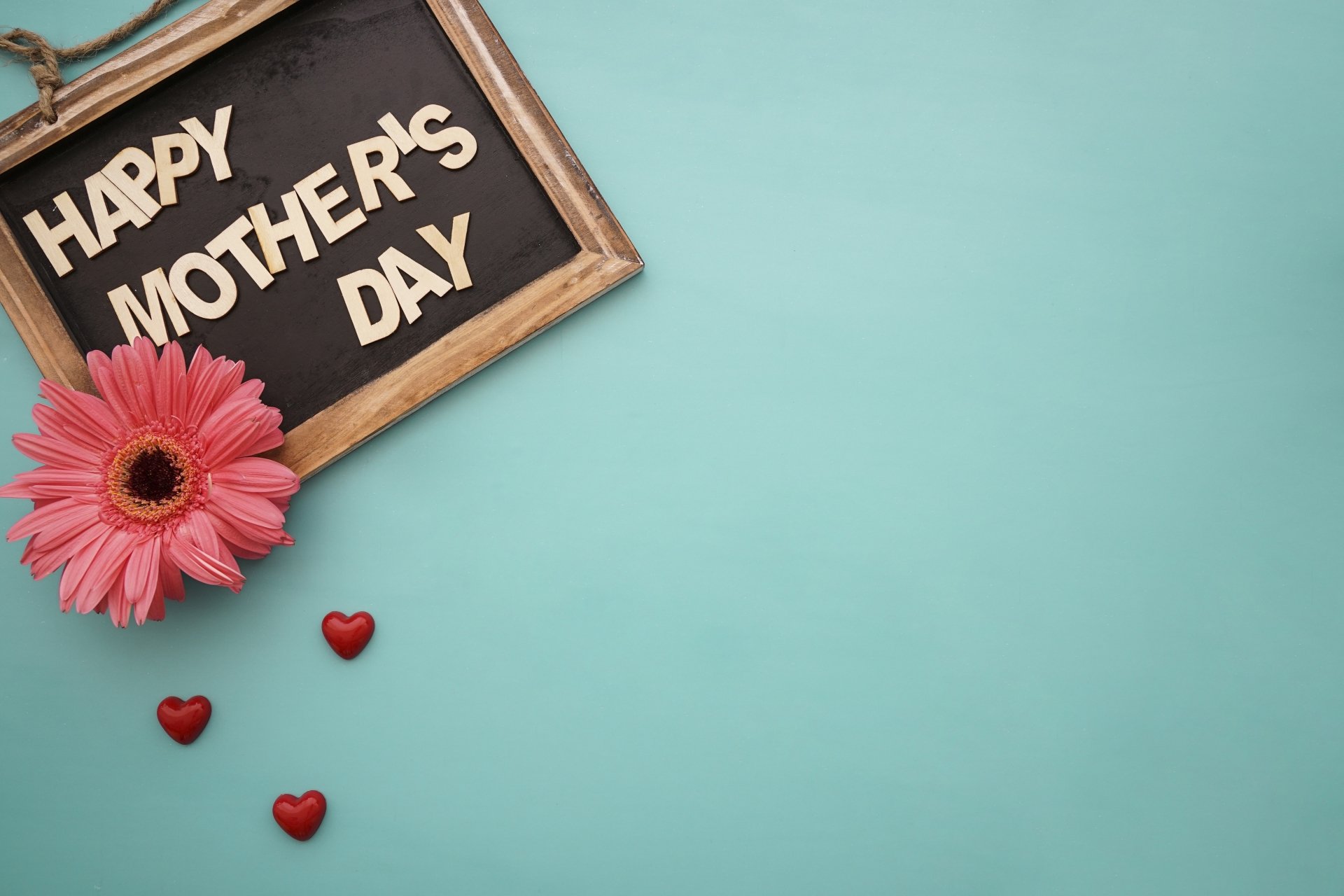 4K Ultra HD desktop wallpaper featuring a pink flower, small red hearts, and a chalkboard sign reading Happy Mother's Day on a light blue background.