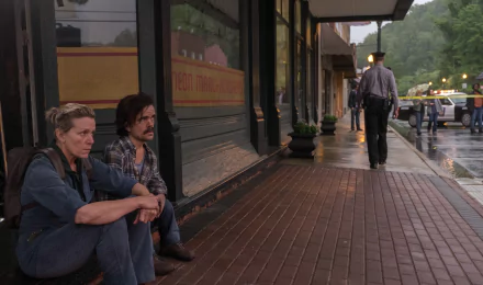 HD wallpaper featuring a scene from Three Billboards Outside Ebbing, Missouri with Frances McDormand and Peter Dinklage sitting on a sidewalk.