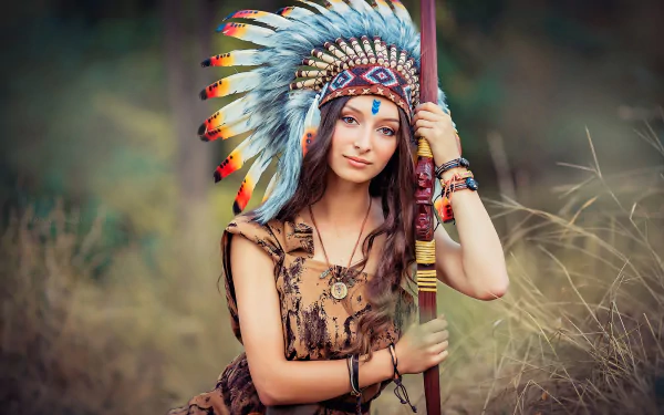 Brunette woman with long hair and brown eyes wearing a feathered headdress, posing in nature. The image features an Asian model with depth of field effect and is an HD desktop wallpaper background.