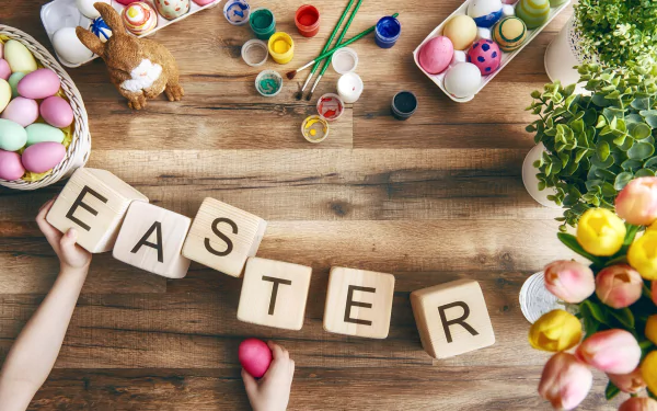 HD still life desktop wallpaper featuring colorful Easter eggs, paint jars, flowers, and wooden blocks spelling EASTER on a rustic wooden table celebrating the holiday.