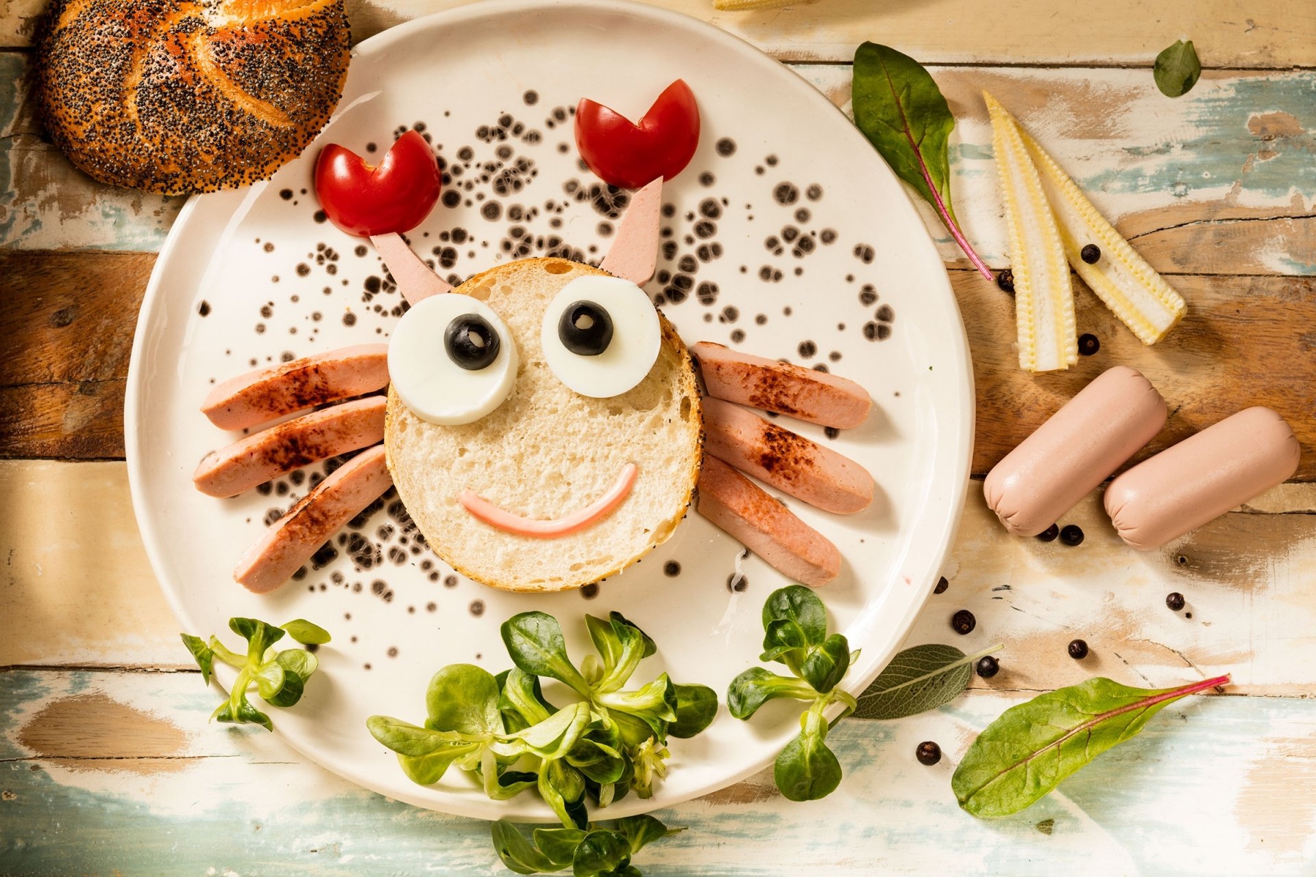 HD PC desktop wallpaper of a playful still life featuring a humorous crab face made from sausage, bread, and olives on a white plate with greens and condiments.