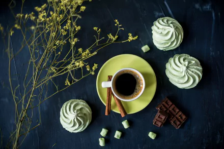 A still life featuring a cup of coffee on a saucer, surrounded by green meringues, pieces of chocolate, and delicate sprigs, set against a dark background. HD desktop wallpaper.