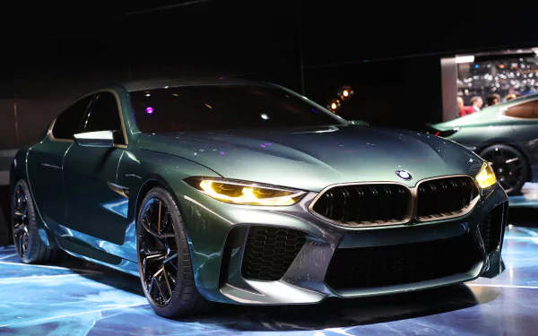 BMW M8 Gran Coupe in metallic green, front three-quarter view with headlights on under showroom lights — high-detail 5K Ultra HD vehicle wallpaper/background.