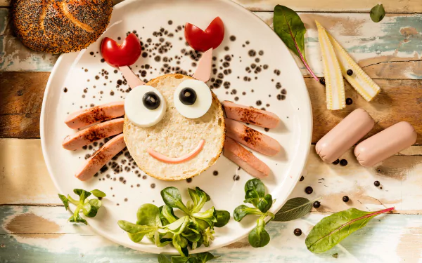 HD PC desktop wallpaper of a playful still life featuring a humorous crab face made from sausage, bread, and olives on a white plate with greens and condiments.
