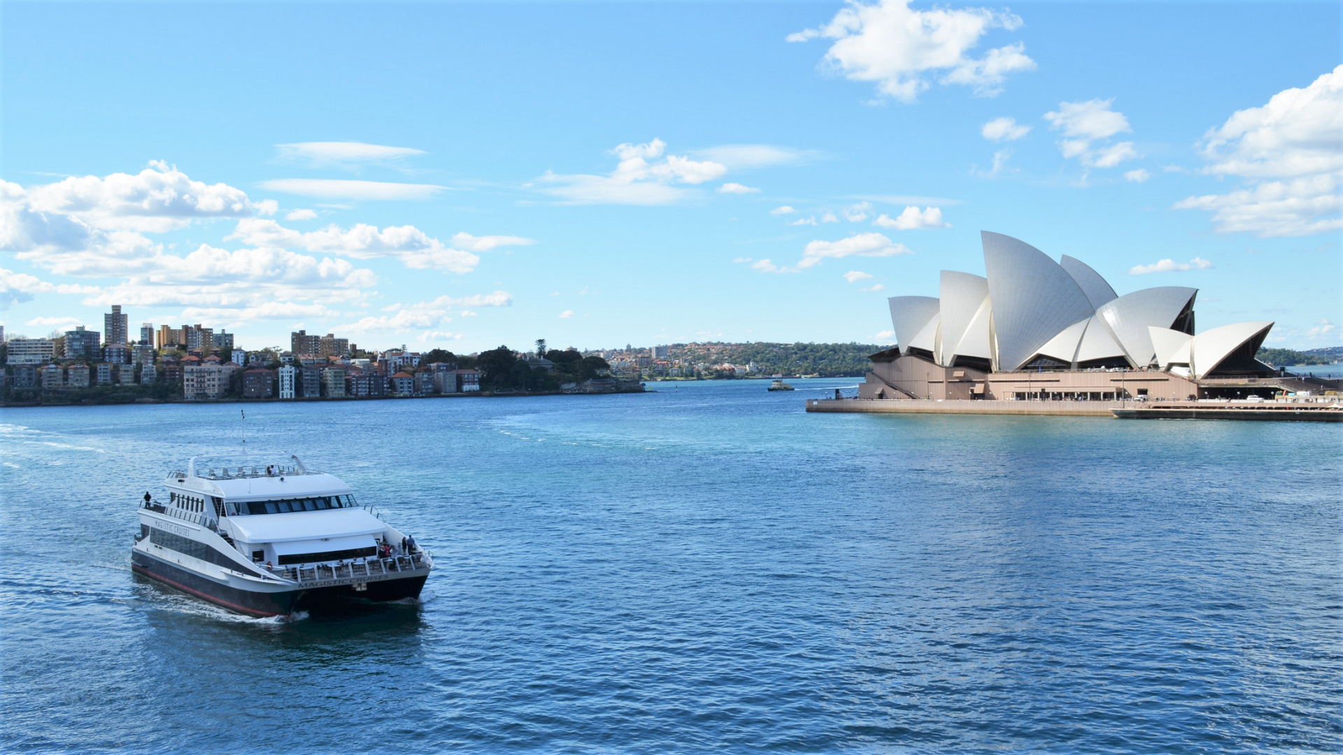 HD desktop wallpaper showing a ferry on Sydney Harbour with the iconic Sydney Opera House and city skyline in Australia under a bright blue sky.