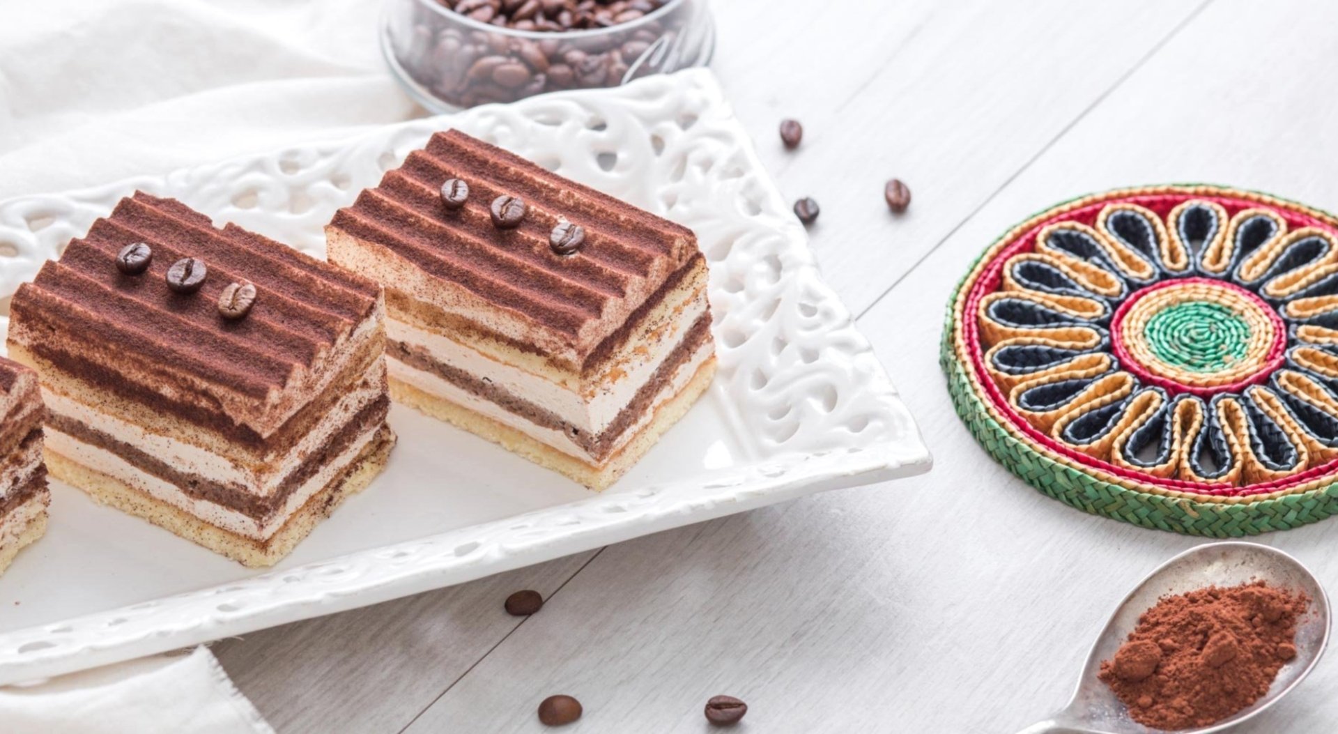 HD desktop wallpaper featuring two layered chocolate pastries on a white plate, surrounded by coffee beans and cocoa powder, highlighting dessert and food themes.